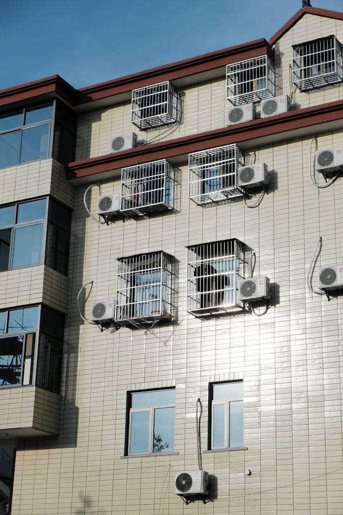 Exterior of a building with multiple air conditioners and window cages.